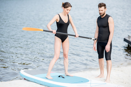 Male coach teaching young woman to surf on the standup paddleboard keeping balance on the boardの写真素材