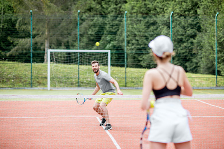 Young couple in white sports wear playing tennis on the tennis court outdoorsの写真素材