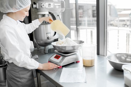 Woman confectioner in uniform weighing ingredients for pastry working at the bakery manufacturingの写真素材
