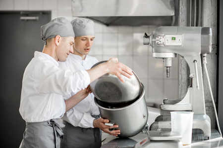 Two handsome confectioners mixing ingredients in bowls for baking at the manufacturingの写真素材