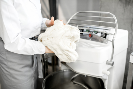 Woman mixing dough with professional kneader machine at the manufacturingの写真素材