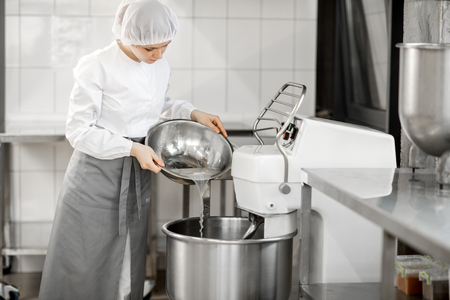 Woman mixing ingredients in the kneader machine standing at the bakery manufacturingの写真素材
