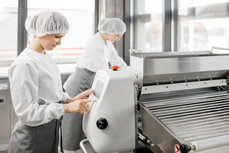 Women in uniform working with dough rolling machine at the bakery manufacturing