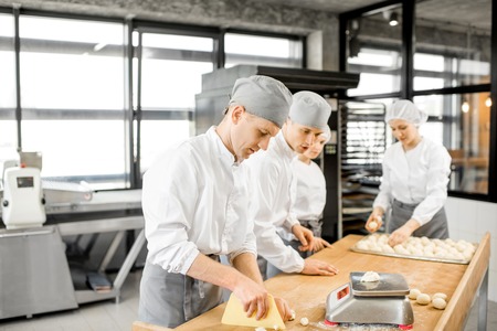 Group of young workers in uniform forming dough for baking on the wooden table standing together at the modern manufacturingの写真素材