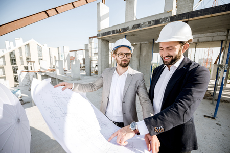 Two business men or engeneers working with house drawings on the structure during the construction process outdoorsの写真素材