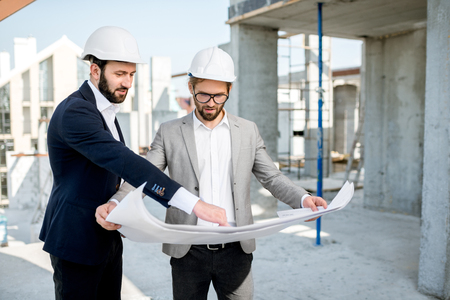 Two business men or engeneers working with house drawings on the structure during the construction process outdoorsの写真素材