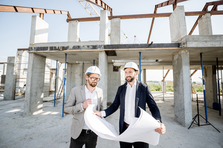 Two business men or engeneers working with house drawings on the structure during the construction process outdoorsの写真素材