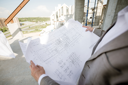 Man holding house plan drawings on the structure outdoorsの写真素材
