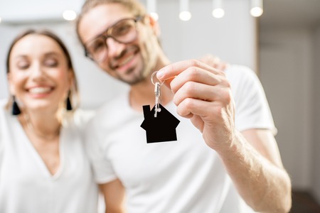 Portrait of a young and happy couple dressed in white t-shirts holding home keys indoorsの写真素材