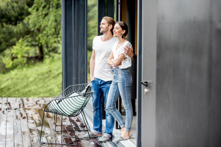 Young couple dressed in white shirts and jeans standing together outdoors on the terrace of the modern houseの写真素材