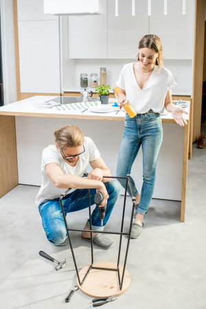 Young lovely couple doing house chores assembling a new chair at the kitchen of the modern apartment