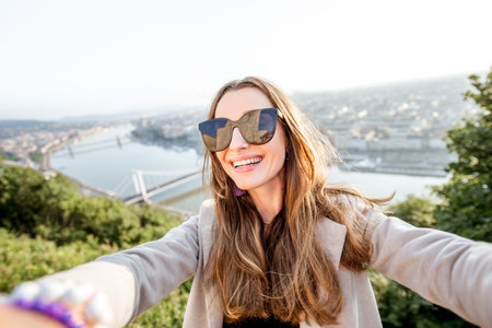 Young pretty woman making selfie photo on the beautiful cityscape background in Budapest city,...