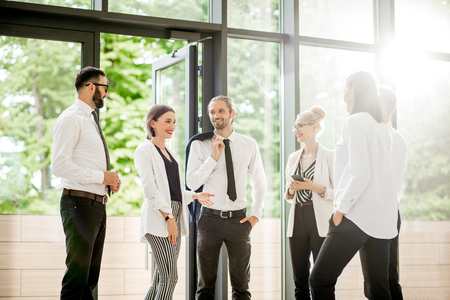 Business people strictly dressed in white having a conversation standing together at the office hall with sunlight indoorsの写真素材