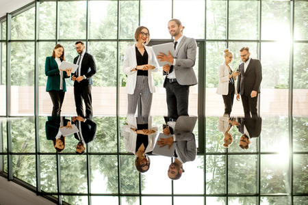Business people standing with gadgets at the modern office hall with window on the background overlooking on the park. View directly with reflection from the tableの写真素材