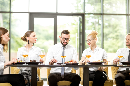 Business people dressed in white shirts having business lunch sitting in a row at the table in the modern restaurantの写真素材