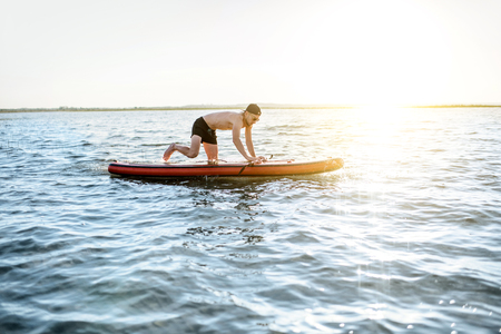 Man jumping on the paddleboard swimming on the lake during the morning lightの写真素材