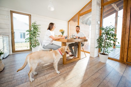 Young couple having a breakfast sitting with dog in the dining room in the wooden country houseの写真素材