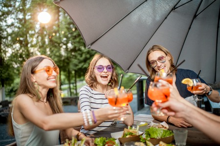 Young friends having fun together clinking glasses during the festive lunch outdoors in the park cafeの写真素材
