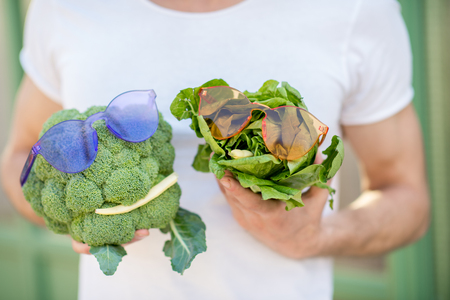 Holding broccoli and lettuce with sunglasses and bean in form of the head on the white t-shirt background, healthy food conceptの写真素材