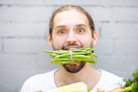 Close portrait of a handsome man biting green beans on the brick wall backgroundの写真素材