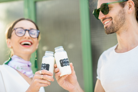Young vegetarian couple drinking oat and almond milk in bottles standing together on the green backgroundの写真素材