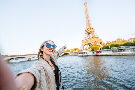 Young woman tourist making selfie photo with Eiffel tower on the background from the boat during the sunset in Parisの写真素材