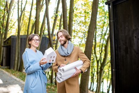 Creative couple of architects or designers standing with drawings and house model outdoors in the forestの写真素材
