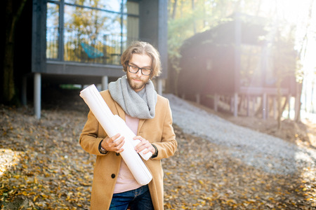 Portrait of a handsome man architect standing with drawings in front of the modern houses in the forestの写真素材