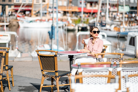 Young woman enjoying coffee sitting at the cafe outdoors near the harbour in Honfleur old town, Franceの写真素材