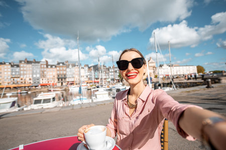Young woman making selfie photo sitting at the cafe outdoors near the harbour in Honfleur old town, Franceの写真素材