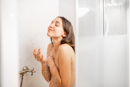 Young and beautiful woman washing her face, taking a shower in the white cabinの写真素材