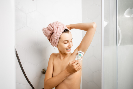 Woman shaving her underarm after the shower standing in the white shower cabinの写真素材