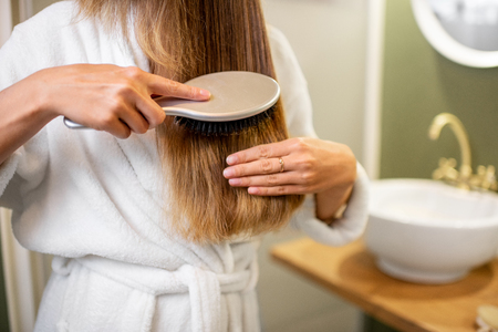 Woman combing hair with brush in the bathroom, close-up view with no faceの写真素材