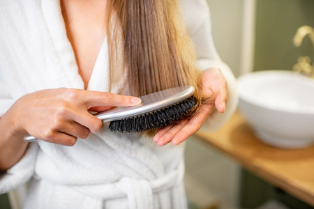 Woman combing hair with brush in the bathroom, close-up view with no faceの写真素材