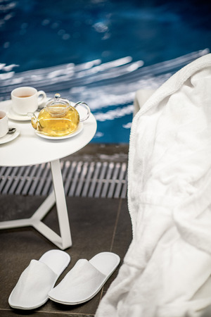 Close-up view on a poolside with tea set and bathrobe on the blue water background indoorsの写真素材