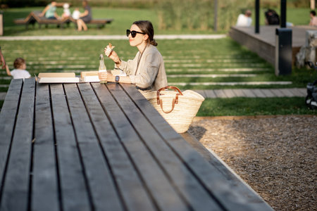 Young woman having a snack with pizza sitting outdoors at the modern public parkの写真素材