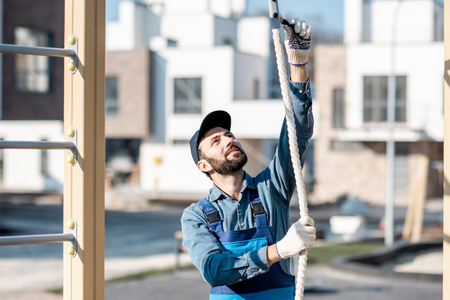 Handsome workman in uniform mounting rope for climbing on the playground outdoorsの写真素材