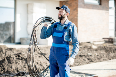 Portrait of a handsome electrician in uniform with power cable for the network on the construction siteの写真素材