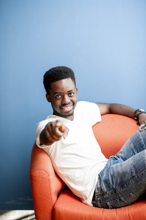 Emotional portrait of a young african man dressed in white t-shirt and jeans sitting on the chair on...