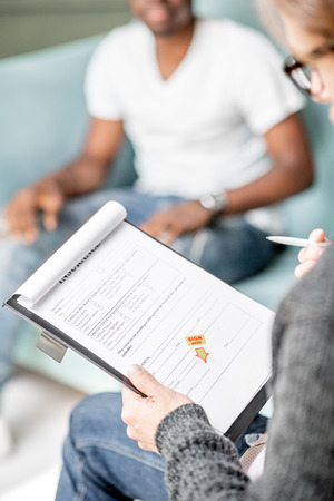 Psychologist filling documents during a psychological session with african man in the officeの写真素材
