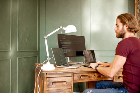 Young programmer writing a program code sitting at the workplace with three monitors in the office...