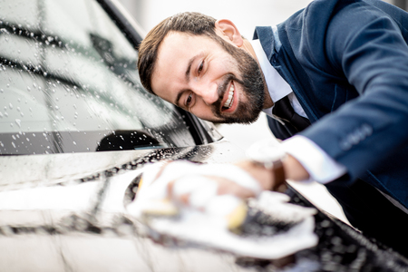 Elegant businessman dressed in the suit washing his car with yellow sponge and foam on a self service car washの写真素材