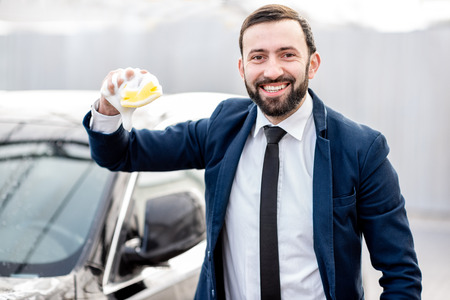 Portrait of a happy businessman in the suit holding sponge for car wash outdoorsの写真素材