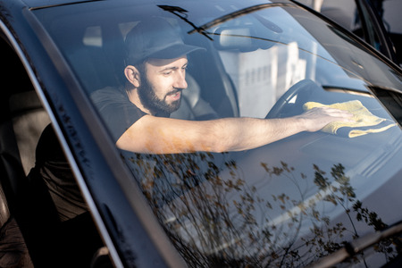 Professional washer wiping car panels with yellow microfiber, view through the windshieldの写真素材