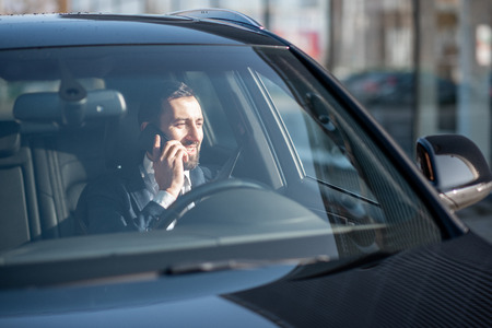 Businessman talking with phone while driving a luxury car, view from the outside through the windshieldの写真素材