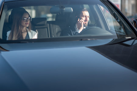 Businessman talking with phone while driving a luxury car with woman, view from the outside through...
