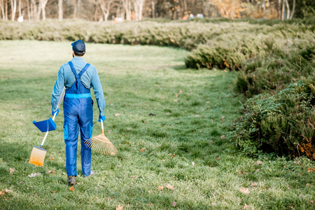 Professional sweeper or gardener in working uniform walking with cleaning tools in the gardenの写真素材