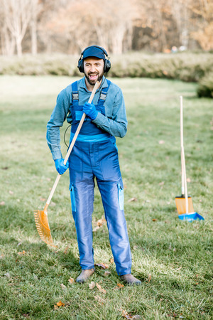 Professional male sweeper or gardener in uniform listening to the music with headphones while cleaning the gardenの写真素材
