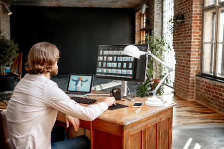 Young male photographer working with womans portraits sitting at the working place with two computers in the studioの写真素材