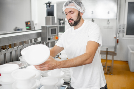 Man in uniform forming cheese into the plastic molds putting them under the press at the cheese manufacturingの写真素材
